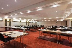 Ein Konferenzraum mit mehreren Tischen, Stühlen und Teppichboden.