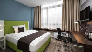Ein Hotelzimmer mit Bett, Schreibtisch, Stuhl, Fernseher und einem Fenster mit Vorhängen.