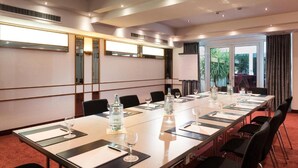 Un salón de conferencias con una mesa grande, sillas y un amplio ventanal con cortinas.
