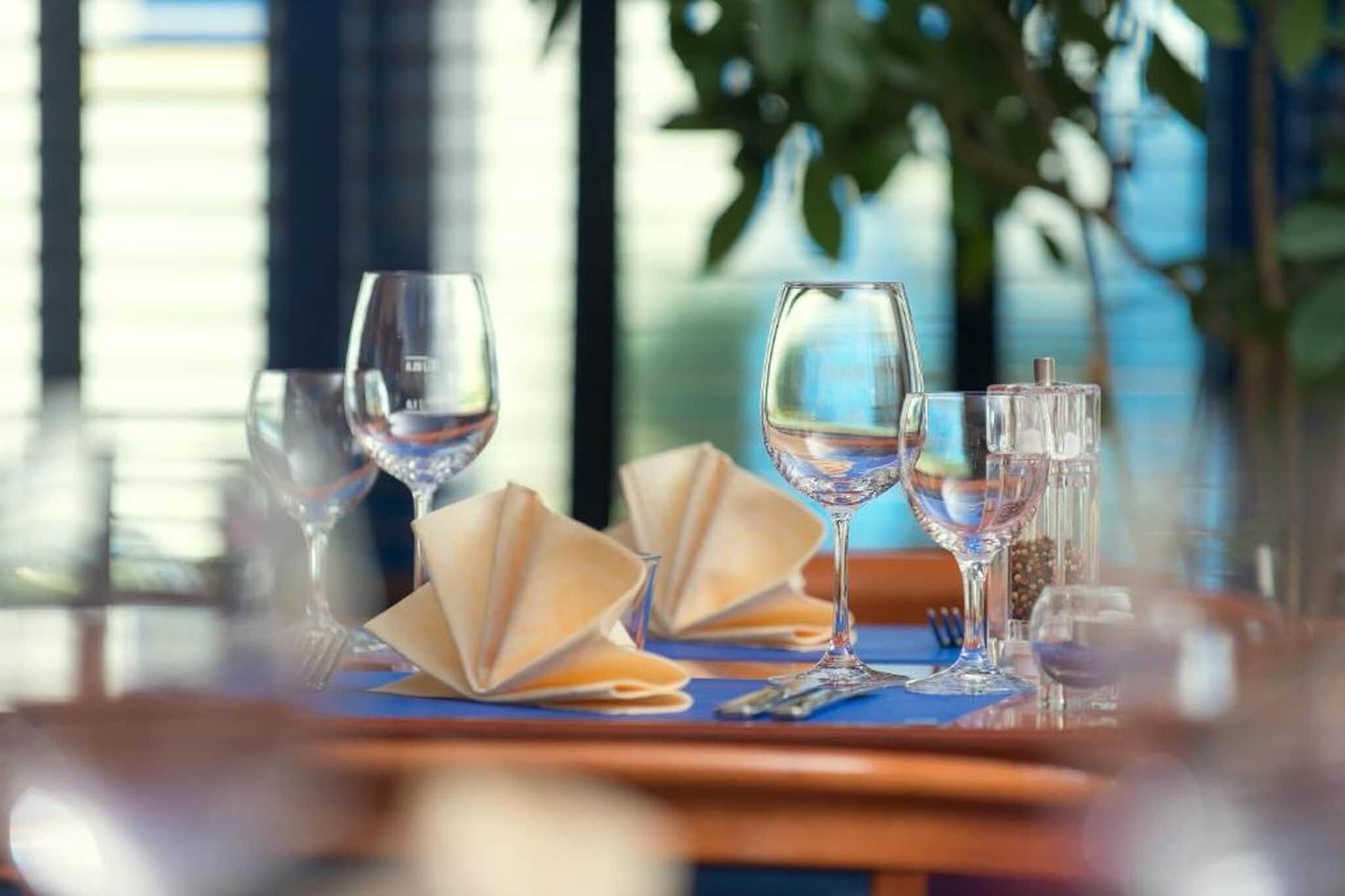 Ein Esstisch mit klarem Glasgeschirr, Servietten und einer blauen Tischmatte.
