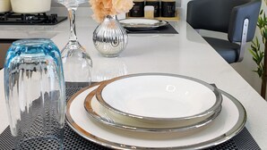 Ett modernt kök med vita skåp, en gasspis, en vas med blommor och en matplats med ett bord dukat för två personer.