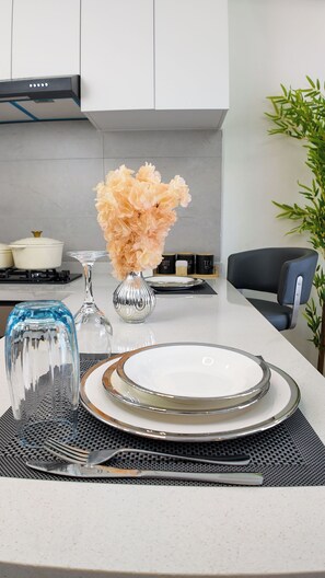 A modern kitchen with white cabinets, a gas stove, a vase with flowers, and a dining area with a table set for two. - Cozy Ikhaya Luxe Silver in Westlands with rooftop gym, heated pool & GTC Views (Nairobi)