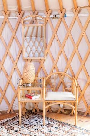 Um quarto com parede de treliça de madeira, uma cadeira de vime, uma luminária trançada e um tapete estampado.
