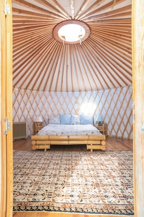 Um interior circular de madeira com uma cama, um tapete estampado e uma parede treliçada.