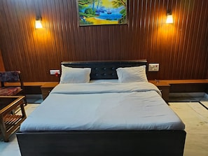 A bedroom with a wooden paneled wall, a bed with white linens, two bedside tables, and a painting above the bed.