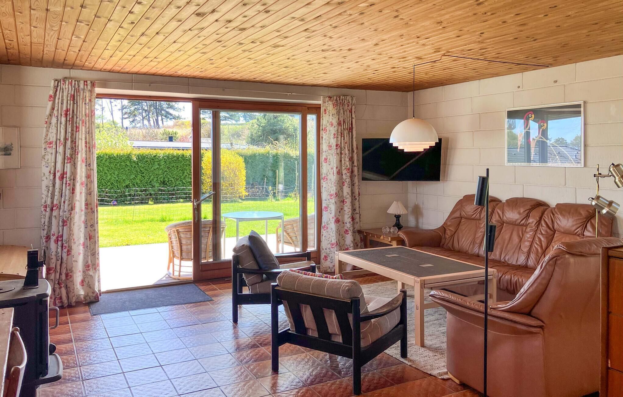 A living room with a sofa, a table, and a TV. There is a sliding glass door leading to a garden.