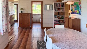 Ein Zimmer mit einem Holzschrank, einem Bücherregal, einem Esstisch und Blick durch eine geöffnete Tür.