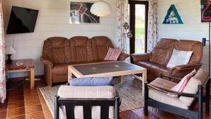 Ein Wohnzimmer mit braunem Ledersofa, einem Holztisch als Couchtisch, einem kleinen Beistelltisch aus Holz und einem schwarzen Sessel.