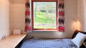 Ein Schlafzimmer mit einem Bett, einem Fenster mit Vorhängen, einem Nachttisch und einer Lampe.