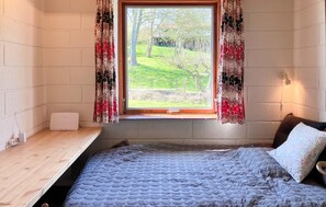 A bedroom with a bed, a window with curtains, a bedside table, and a lamp.