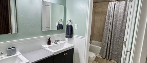 A bathroom with two sinks, a large mirror, a shower curtain, and a toilet.