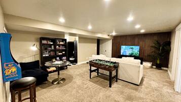 A living room with a foosball table, a sofa, a bookshelf, and a television.