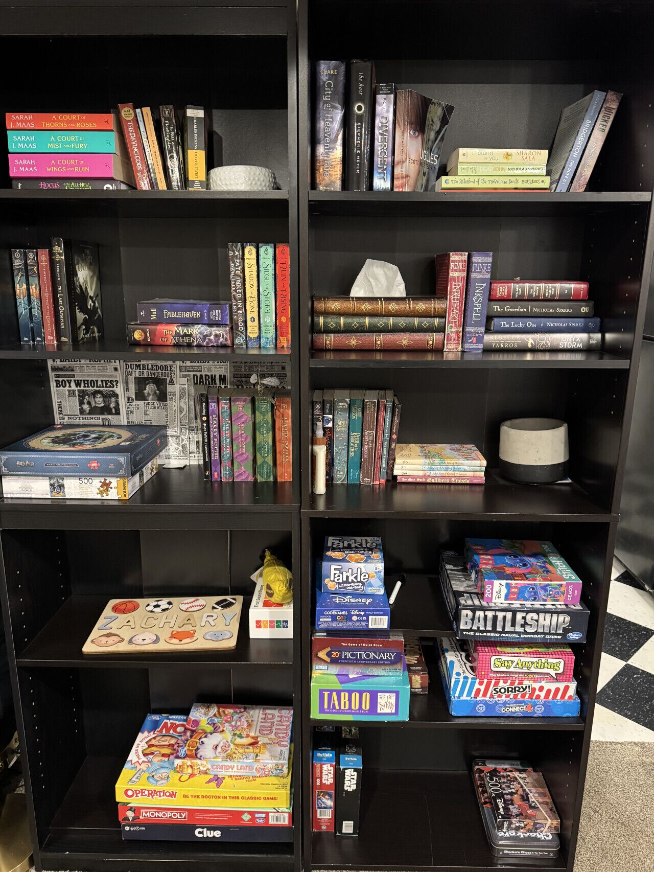 Een boekenplank met verschillende boeken, spellen en een klein wit voorwerp.