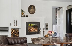 A living room with a fireplace, a dining table, a sofa, and a hallway leading to a kitchen. - 5 bedroom nice home in Kirke Hyllinge (Kirke Hyllinge)