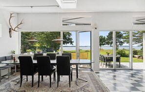 Un comedor moderno con una mesa y sillas de vidrio, un tapete estampado y un ventanal con vistas a un lago.