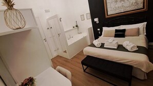 Una habitación de hotel con cama, escritorio, silla, una mesita y una obra de arte colgada en la pared.