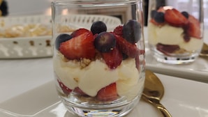Un postre en una copa de vidrio transparente sobre un plato blanco, con una cuchara dorada a un lado.