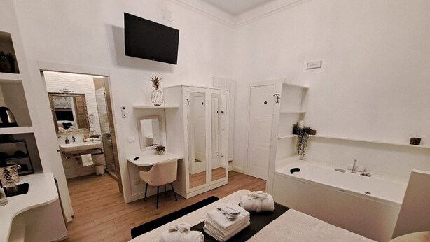Habitación de hotel moderna con cama, escritorio, silla, televisor, baño con lavabo y espejo, y armario.