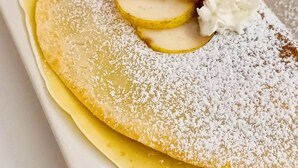 Un plato de postre con un crepe, rebanadas de manzana, bayas, crema batida y azúcar glas.