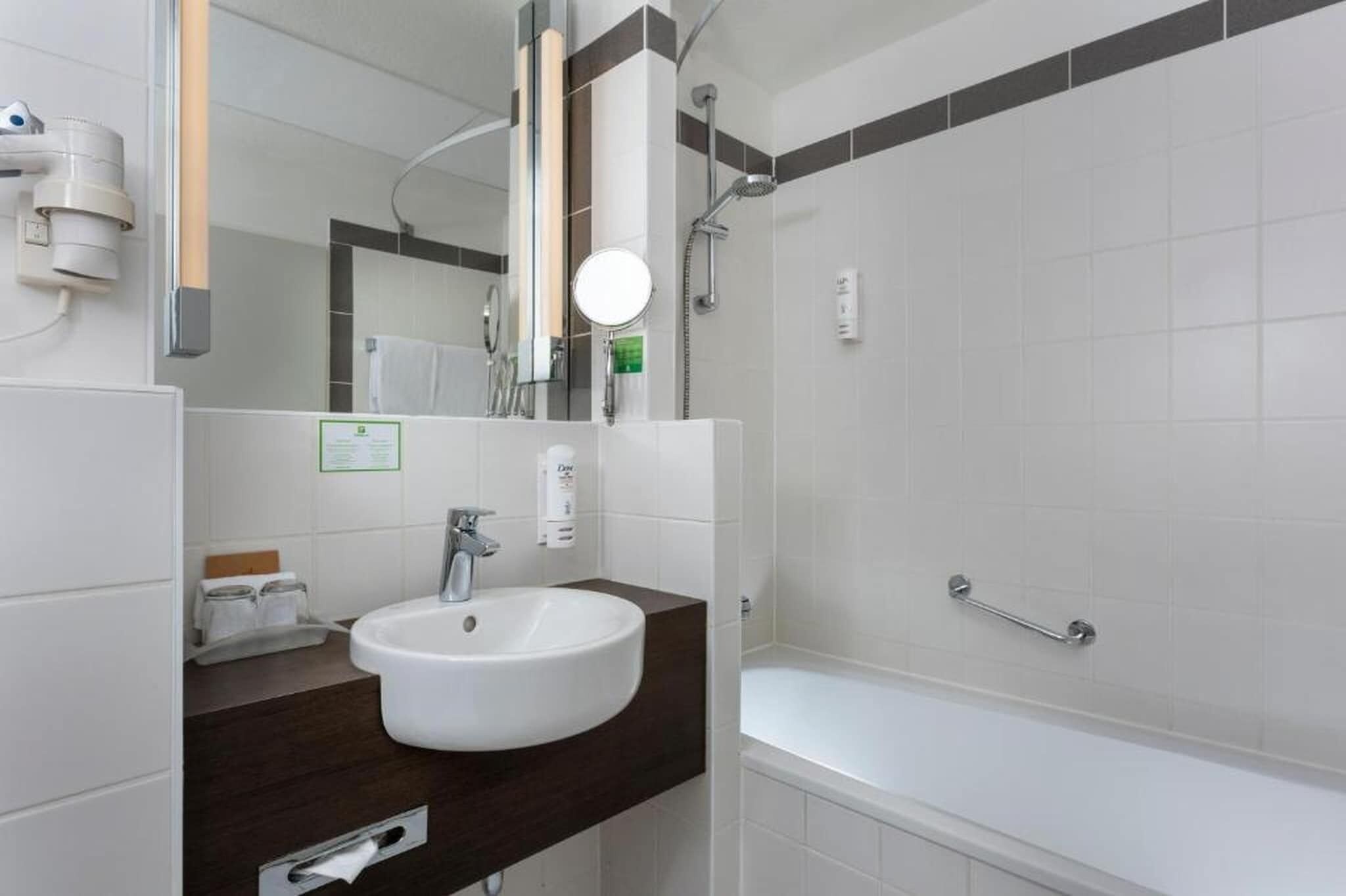 Ein modernes Badezimmer mit einem weißen Waschbecken, einer dunklen Arbeitsplatte und einem Duschbereich.