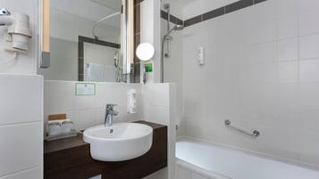 Ein modernes Badezimmer mit einem weißen Waschbecken, einer dunklen Arbeitsplatte und einem Duschbereich.