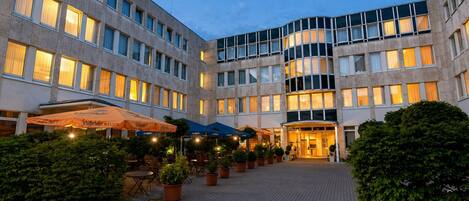 En hotelgård med udendørs siddepladser, plantekasser og en godt oplyst indgang.