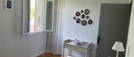 A bedroom with a bed, a bedside table, a lamp, a window with curtains, a door, and wall-mounted pictures.