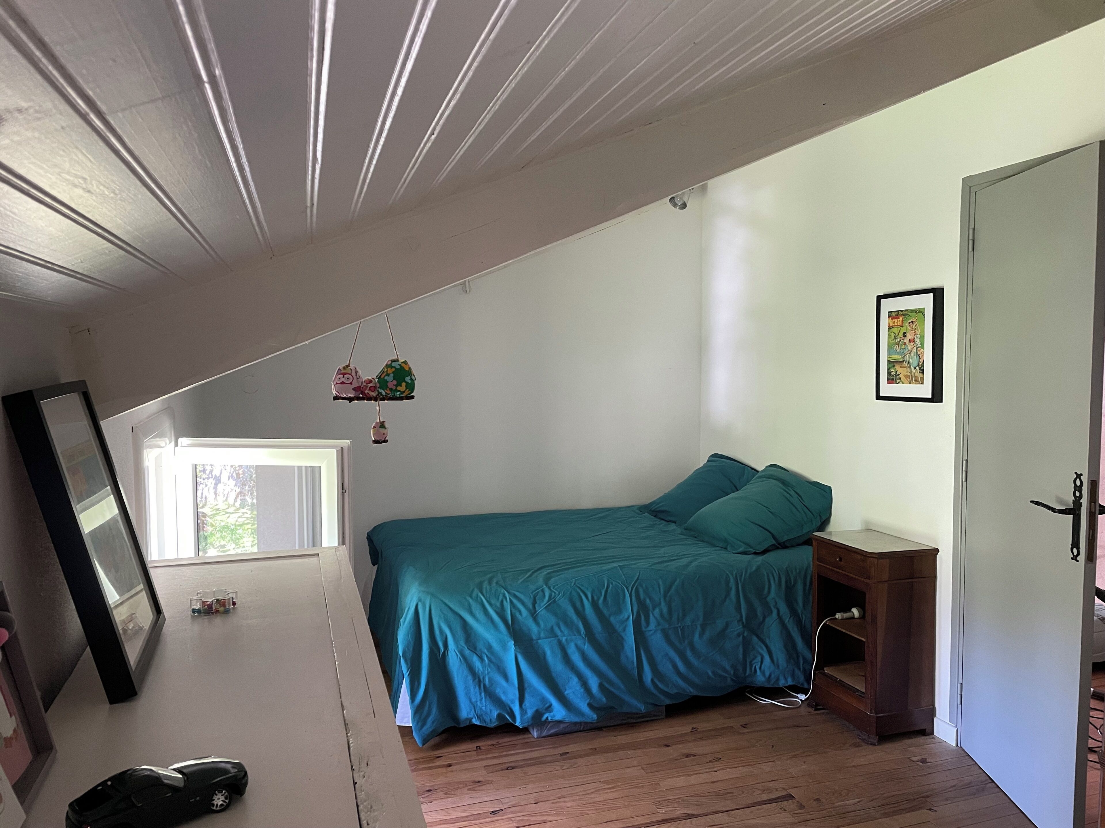 Un dormitorio con cama, cómoda de madera, lámpara colgante y una puerta.