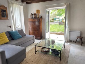Ett vardagsrum med en soffa, ett soffbord i glas, ett träskåp och utsikt över en uteplats.