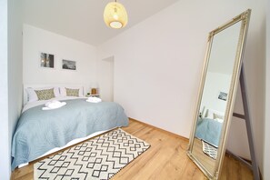 Quarto com cama, espelho grande, luminária na parede e tapete estampado.