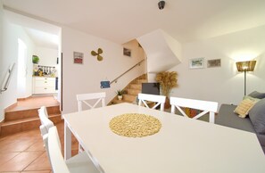 Uma área de refeições com uma mesa branca, cadeiras e um jogo americano trançado.