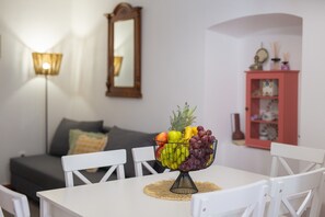 A dining table with a fruit bowl, white chairs, a gray sofa, a mirror, and a pink cabinet in a room. - Vacation home Paola near the beach (Vrbnik)