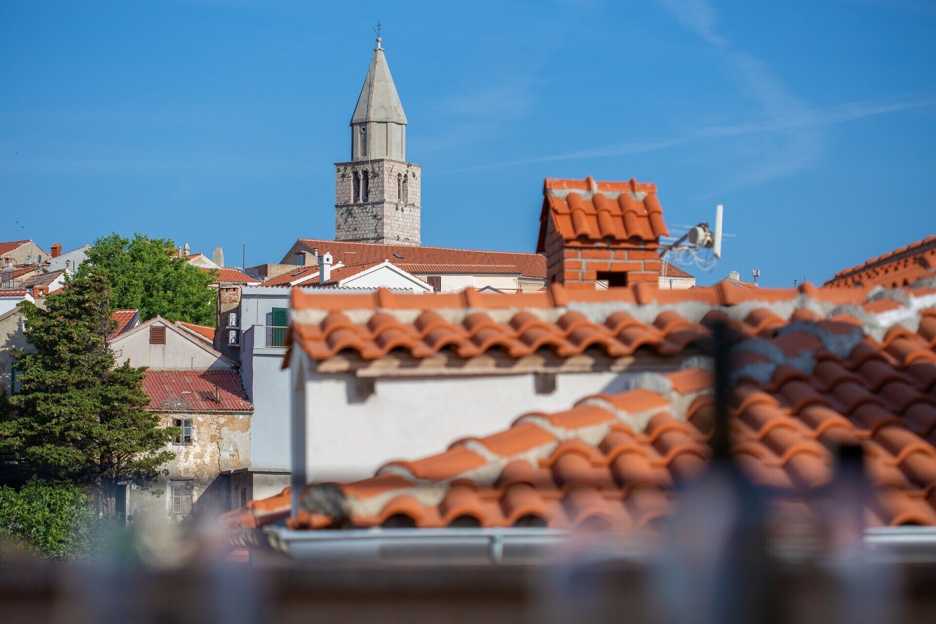 A building with a prominent tower, red-tiled roofs, and a clear blue sky.