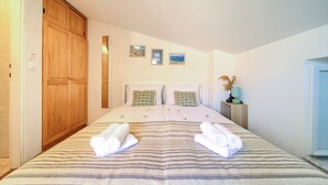 Een slaapkamer met een groot bed, een houten garderobe en twee aan de muur bevestigde foto's.