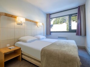 A hotel room with a bed, bedside tables, a window with curtains, and a view of greenery outside. - 1 BR Apartment in Flaine (Araches-la-Frasse)