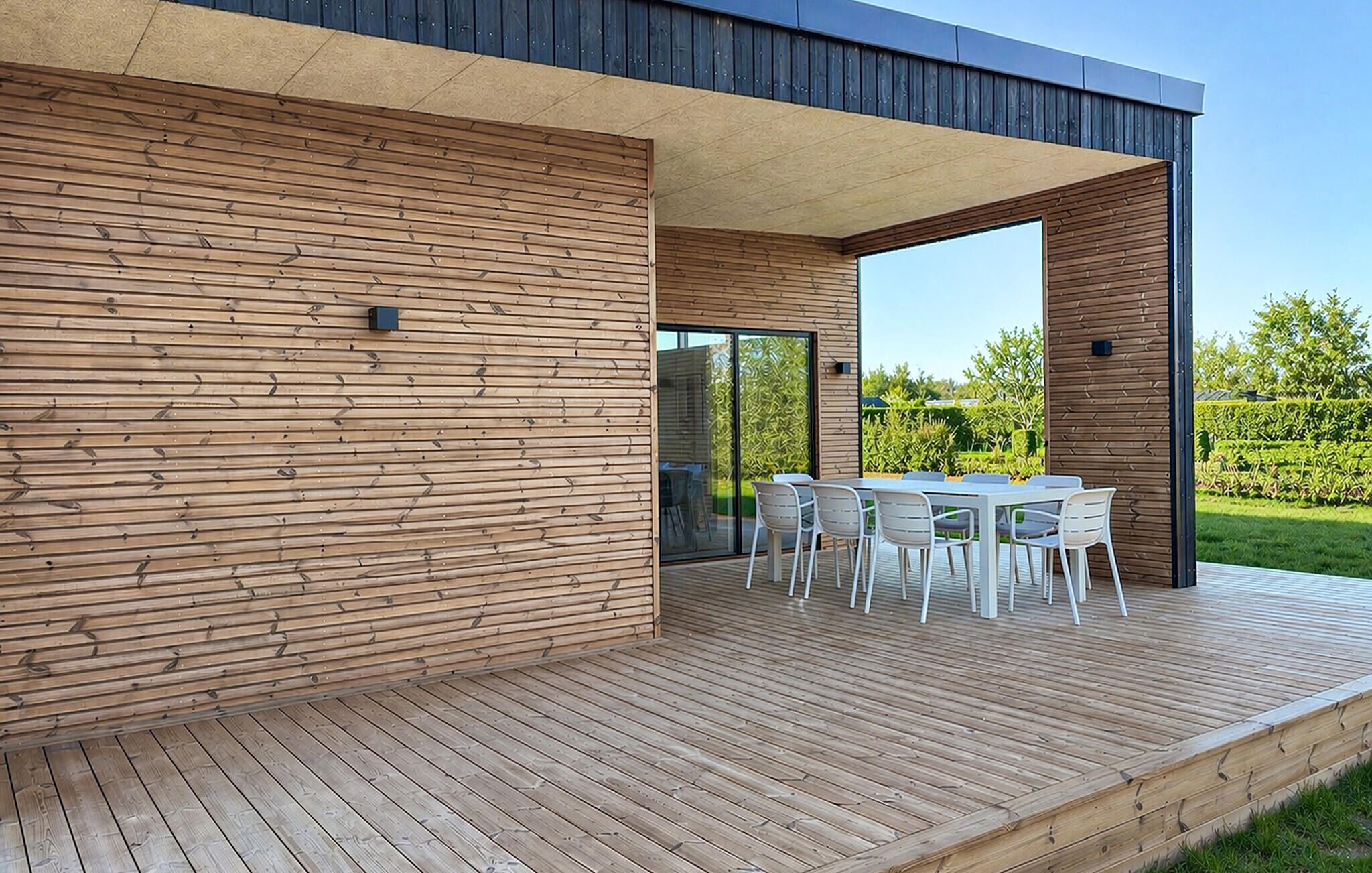 A modern outdoor patio with a wooden deck, a table with chairs, and a glass door leading to a garden.