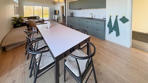 Una cucina moderna con isola centrale, un'area pranzo con un tavolo lungo e sedie, e vista all'esterno tramite ampie finestre.