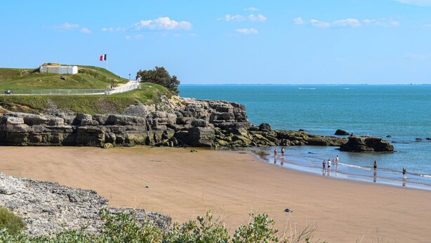 A coastal beach with rocky cliffs, a grassy hill with a structure, and a clear blue sky. - Appartement proche plage (Saint-Palais-sur-Mer)