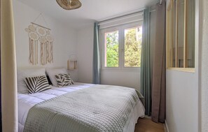 Une chambre à coucher avec un lit, une fenêtre avec des rideaux, un luminaire fixé au mur et un élément décoratif mural.