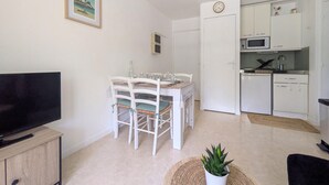 A compact living space with a dining area, kitchenette, and a television on a wooden cabinet. - Appartement proche plage (Saint-Palais-sur-Mer)