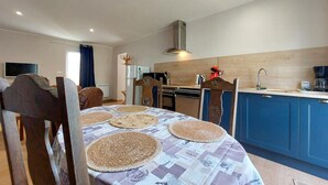 A dining area with a table set for four, a kitchen with blue cabinets, and a modern stove. - Awesome home in Sauzé-entre-Bois with WiFi (Sauzé-entre-Bois)