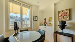 Een moderne kamer met een eettafel, stoelen, een raam met uitzicht op gebouwen en kunst aan de muur.