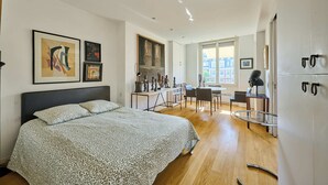 Een slaapkamer met een bed, een bureau en een stoel, een zithoek met een tafel en stoelen, en een uitzicht op gebouwen.