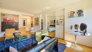 Een moderne woonkamer met een bank, stoelen, een glazen salontafel en kunstwerken aan de muur.