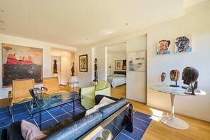 A modern living room with a sofa, chairs, a glass coffee table, and artwork on the walls. - DAUPHINE SQ City island - Elegant Apartment - 1 Bedroom - 1 Bath - Sleeps 2 (Paris)