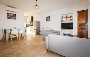 A modern apartment with a dining area, kitchen, living room, and a TV mounted on the wall.