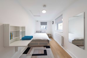 A modern, well-lit bedroom with a bed, a small table, a bookshelf, and a window. - Spacious 4BR Home in Mile End – Amazing Location (Greater London)