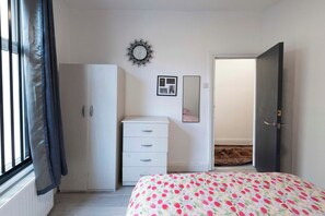 Een slaapkamer met een bed, een kledingkast, een dressoir, een spiegel en een deur naar een andere kamer.