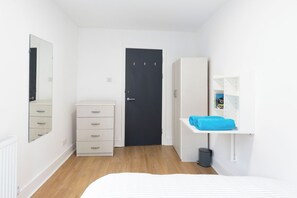 A bedroom with a bed, a wardrobe, a dresser, a door, and a shelf with a towel. - Spacious 4BR Home in Mile End – Amazing Location (Greater London)