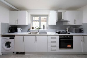 Une cuisine moderne avec des meubles blancs, un lave-linge encastré, un four à micro-ondes et une cuisinière.